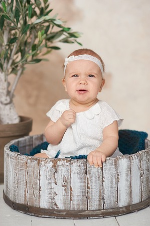 Adorable Ten month old newborn baby girl sitting in a wooden bucket. Copy space. Portrait of toddler indoor.の写真素材