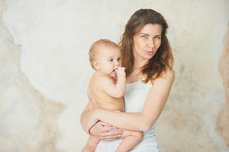beautiful young mother with baby girl in her arms. The concept of a happy family, motherhood. mother playing with baby in room. fingers in the mouth. teething. peristalsisの写真素材