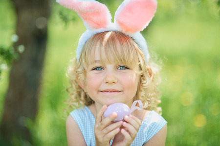 Cute funny girl with Easter eggs and bunny ears at garden. easter concept. Laughing child at Easter egg hunt. Child in park with eggs, spring conceptの写真素材