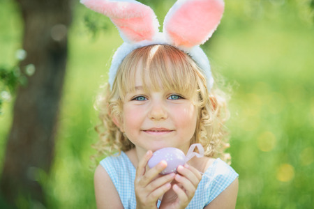 Cute funny girl with Easter eggs and bunny ears at garden. easter concept. Laughing child at Easter egg hunt. Child in park with eggs, spring concept