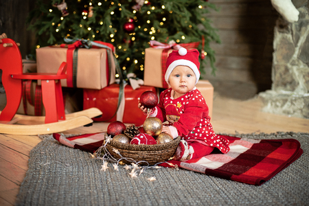 The little girl under the Christmas tree. baby girl in Santa Claus hat with gifts under Christmas tree at fireplace with piggy toyの写真素材