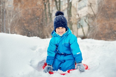 child rolls down a snow hill. Boy sliding down snow hill in winter. Kids play outside. Winter fun concept.の写真素材