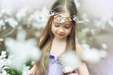fairy tale girl. Portrait of mystic elf child. Cosplay character. Portrait of an elf in a blooming garden. A girl with long ears touchesの写真素材