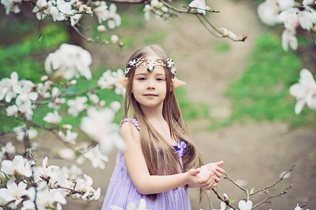 fairy tale girl. Portrait of mystic elf child. Cosplay character. Portrait of an elf in a blooming garden. A girl with long ears touches the flowers.の写真素材
