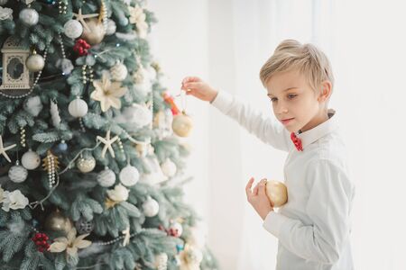 Child decorating Christmas tree at home. Boy hangs Christmas balls on tree. Christmas Eve concept. smiling handsome boy stands near a Christmas tree.の写真素材