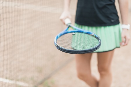 Front view of beautiful young female tennis player. Close up of a player holding tennis racket on clay court trainingの写真素材