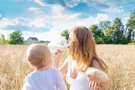 Mother and daughter in wheat field. Happy Family outdoors. healthy child with mother on picnic with bread and milk in golden cereal fieldの写真素材