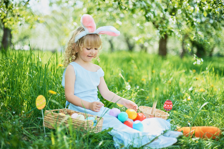 Cute funny girl with Easter eggs and bunny ears at garden. easter concept. Laughing child at Easter egg hunt. Child in park with basket full of eggs, spring conceptの写真素材