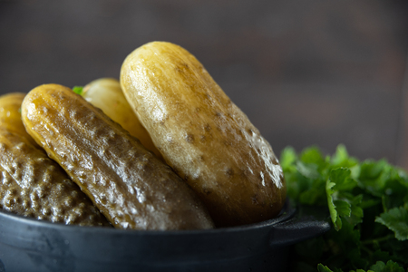 Marinated cucumbers gherkins. Pickled cucumbers with parsley in a bowl against dark rustic background. Salted cucumbers - one of the traditional Slavic dishes, as well as German cuisine Salzgurken .の写真素材