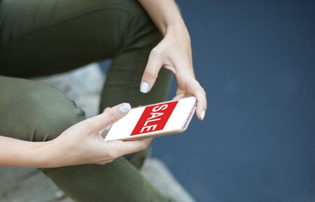 Close-up of female hands on smartphone with inscription - sale. Girl is shopping online. Young woman...
