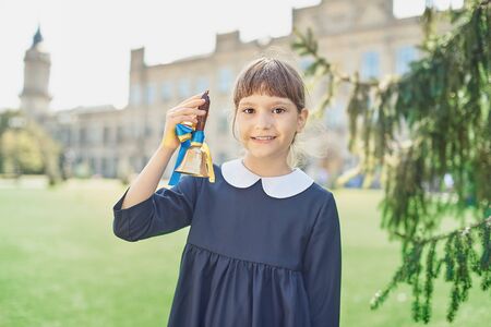 Portrait of beautiful young Schoolgirl on background school. Farewell Bell. day of knowledge. beginning of school year. Child with bellの写真素材