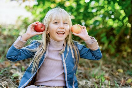Girl with Apple holding her face in Apple Orchard. Beautiful Girl Eating Organic Apple in the Orchard. Harvest Concept. Garden, Toddler eating fruits at fall harvest.の写真素材