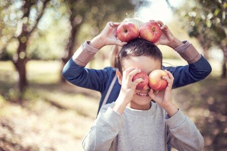Boy with Apple holding on head in the Apple Orchard. Beautiful Girl Eating Organic Apple in the...