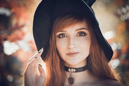 Close up portrait of Halloween Beautiful young Witch girl in witches hat on spooky dark magic forest...