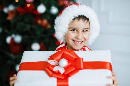 Happy excited child holding christmas gift box. Boy giving a Christmas present in decorated room. christmas and people concept. New Year Happy holidays. kid satisfied with present.の写真素材