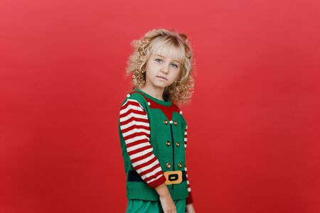 Merry Christmas Little girl in Santa elf helper costume on bright red vivid color background. Red and green. Portrait of lovely elf child. Copy spaceの写真素材