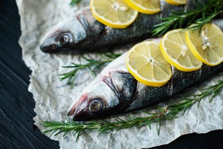 Raw fish seabass. Two Raw fish fillet with spices, herbs, lemon and salt on paper black stone...