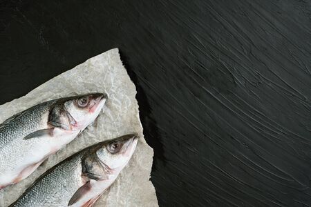 Raw fish seabass. Two Raw fish fillet on paper black stone background ready for cooking, food...