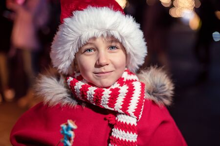 Child on christmas market. cute lovely girl in red hat standing at street happy about gingerbread cookies. Traditional leisure for families on xmas holidays. Family, tradition, holiday conceptの写真素材