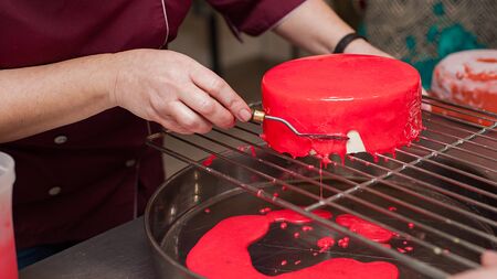 French mousse cakes with mirror glaze. Modern european dessert. Preparation of tasty mousse cake. cooking, baking and confectionery concept. Culinary master class. Female chef lays out cake on plateの写真素材