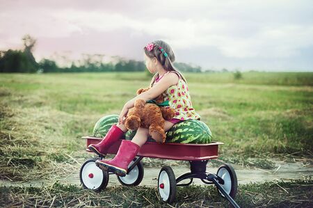 girl eating watermelon. happy child in the field. Summer mood. girl with red wagon full of watermelonの写真素材