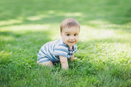 7 month child crawls on grass in yard, Concept education of children, children's goods. Naked legs. Healthy baby. Childhood.の写真素材