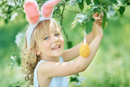 Cute funny girl with Easter eggs and bunny ears at garden. easter concept. Laughing child at Easter...