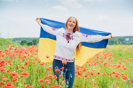 woman prays holding Ukraine flag in her hands in field. Ukraine's Independence Day. Flag Day. Constitution day. Girl in traditional embroidery with flag of Ukraine. 24 August. Patriotic holiday.の写真素材