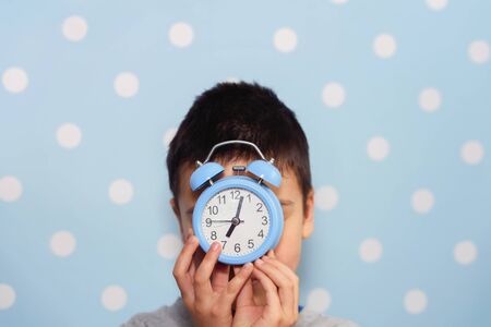 Cute little boy with alarm clock, People, school, time and lifestyle concept. sleepyhead or early bird. Sleeping child with alarm clock in front of face. Back to school. Copyspaceの写真素材
