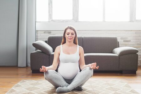 Pregnancy yoga. Beautiful expectant mother doing yoga at home. sitting in lotus Relaxation. healthcare conceptの写真素材