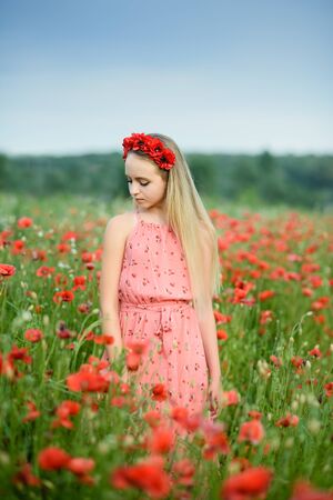 Ukrainian Beautiful girl in poppies field and wheat. outdoor portrait. Child collecting poppies and cornflower in summer field. Blooming Poppies memory symbol.の写真素材