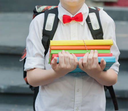 Portrait of a young school boy standing with books and red apple on background autumn park. Farewell Bell. day of knowledge. beginning of the school year. first-graderの写真素材