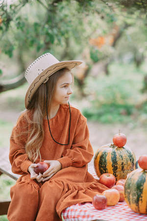 Autumn portrait of child on pumpkin patch on cold autumn day with a lot of pumpkins and apples for halloween or thanksgiving. Child picking pumpkin at farm autumn seasonの写真素材