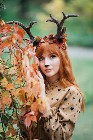 fairy woman with deer horns in autumn forest. Face painting. Beautiful mystery woman. redhead girl with big eyes magical sightの写真素材