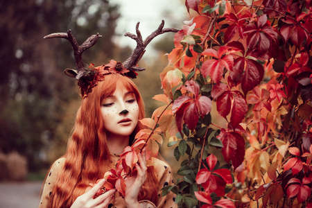 fairy woman with deer horns in autumn forest. Face painting. Beautiful mystery woman. redhead girl with big eyes magical sightの写真素材