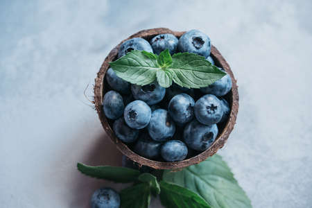Freshly picked blueberries in coconut bowl on dark background. Healthy organic seasonal fruit...