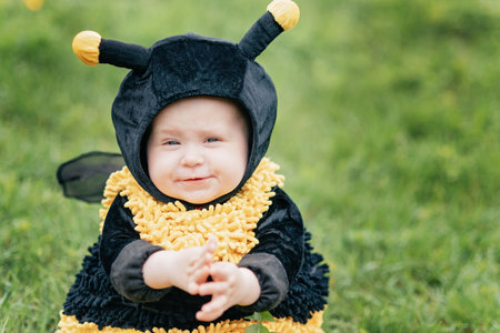 cute and cheerful portrait of little child sitting in blooming flowers of dandelion in yellow bee...