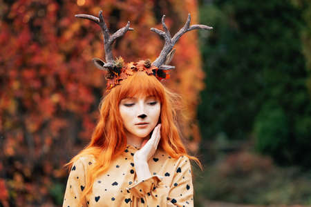 fairy woman with deer horns in autumn forest. Face painting. Beautiful mystery woman. redhead girl with big eyes magical sightの写真素材