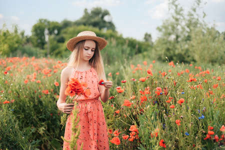 Ukrainian Beautiful girl in poppies field and wheat. outdoor portrait. Child collecting poppies and cornflower in summer field. Blooming Poppies memory symbol.の写真素材