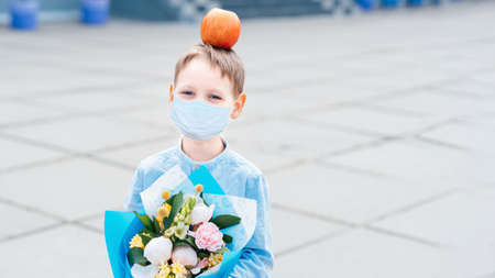 Portrait of schoolboy wearing medicine mask with bouquet in uniform on background school. Farewell...