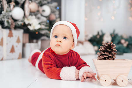 Little child under Christmas tree. baby boy in Santa Claus hat with gifts under Christmas tree with many gift boxes presents. Happy Holidays, New year. Cozy warm winter evening at home. Xmas timeの写真素材