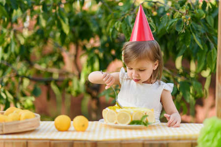 girl eating lemon Birthday cake. Lemonade birthday party at summer park. food, celebration and festive concept. Little child drinks natural lemonade at stand in parkの写真素材