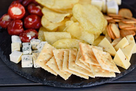 Mix of different snacks and appetizers. Street food plate with set of various kind snacks: bread spicy crackers, french fries and dip, tomatoes, delicious cheese on dark background. antipasto plateの写真素材