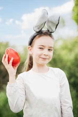 Cute funny girl with Easter eggs and bunny ears at garden. easter concept. Laughing child at Easter...