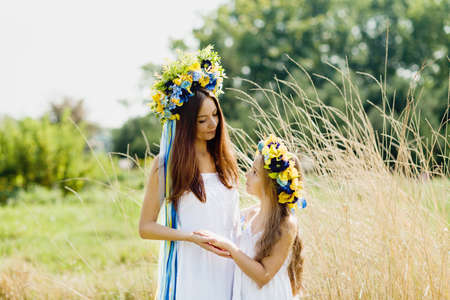 mother and daughter in traditional Ukrainian wreaths in on head blue and yellow flag of Ukraine in field. Ukraine Independence Flag Day. Constitution day. 24 August. Patriotic holiday. Woman and childの写真素材