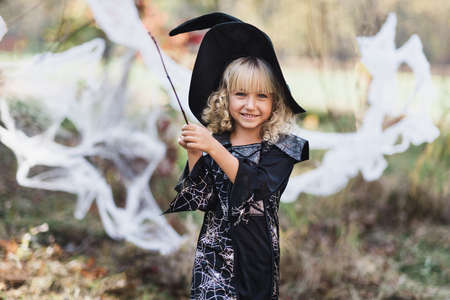 Beautiful girl witch. little girl in whitch costume and hat celebrate Halloween outdoor and have fun. Kids trick or treating. girl witch with magic Book of spells, broomの写真素材