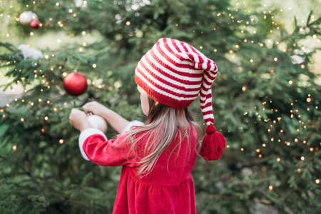 Christmas in july. Child waiting for Christmas in wood in summer. portrait of little girl in red dress decorating christmas tree. winter holidays and people concept. Merry Christmas and Happy Holidaysの写真素材