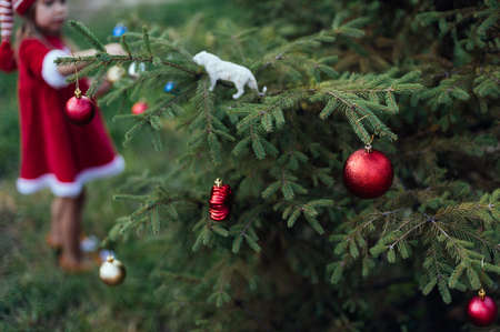 Christmas in july. Child waiting for Christmas in wood in summer. portrait of little girl in red dress decorating christmas tree. winter holidays and people concept. Merry Christmas and Happy Holidaysの写真素材