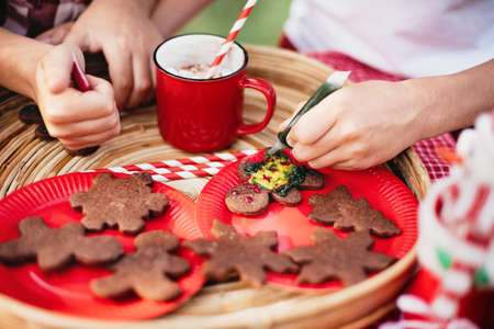 Happy children preparing for Christmas. Two boys and girl in santa hat color gingerbread cookies, drinking hot chocolate outside having fun. kids decorate gingerbread man. Holidays conceptの写真素材