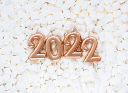 Holiday background Happy New Year 2021. Numbers of year 2022 made by gold candles on white...